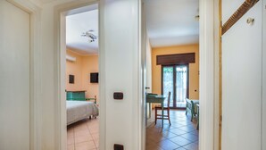 Een gang die leidt naar een slaapkamer met een bed, een groene kast en een televisie aan de muur.