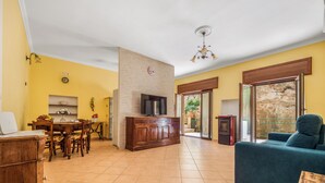 Een woonkamer met een bank, een televisie, een eethoek met een tafel en stoelen, en een keuken met een koelkast en een televisie.