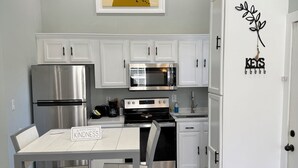 A modern kitchen with white cabinets, stainless steel appliances, and a dining area with a table and chairs. - Wandering Inn FY25 Build. (Monroe)