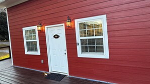 A red wooden house with two windows and a white door, each with a small window above. - Wandering Inn FY25 Build. (Monroe)