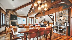 Un'ampia zona giorno con un grande tavolo da pranzo in legno, posti a sedere confortevoli, un camino in pietra e una parete decorata con pietra.