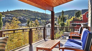 Un terrazzo in legno con tavolo e sedie blu, affacciato su un paesaggio montuoso con case.