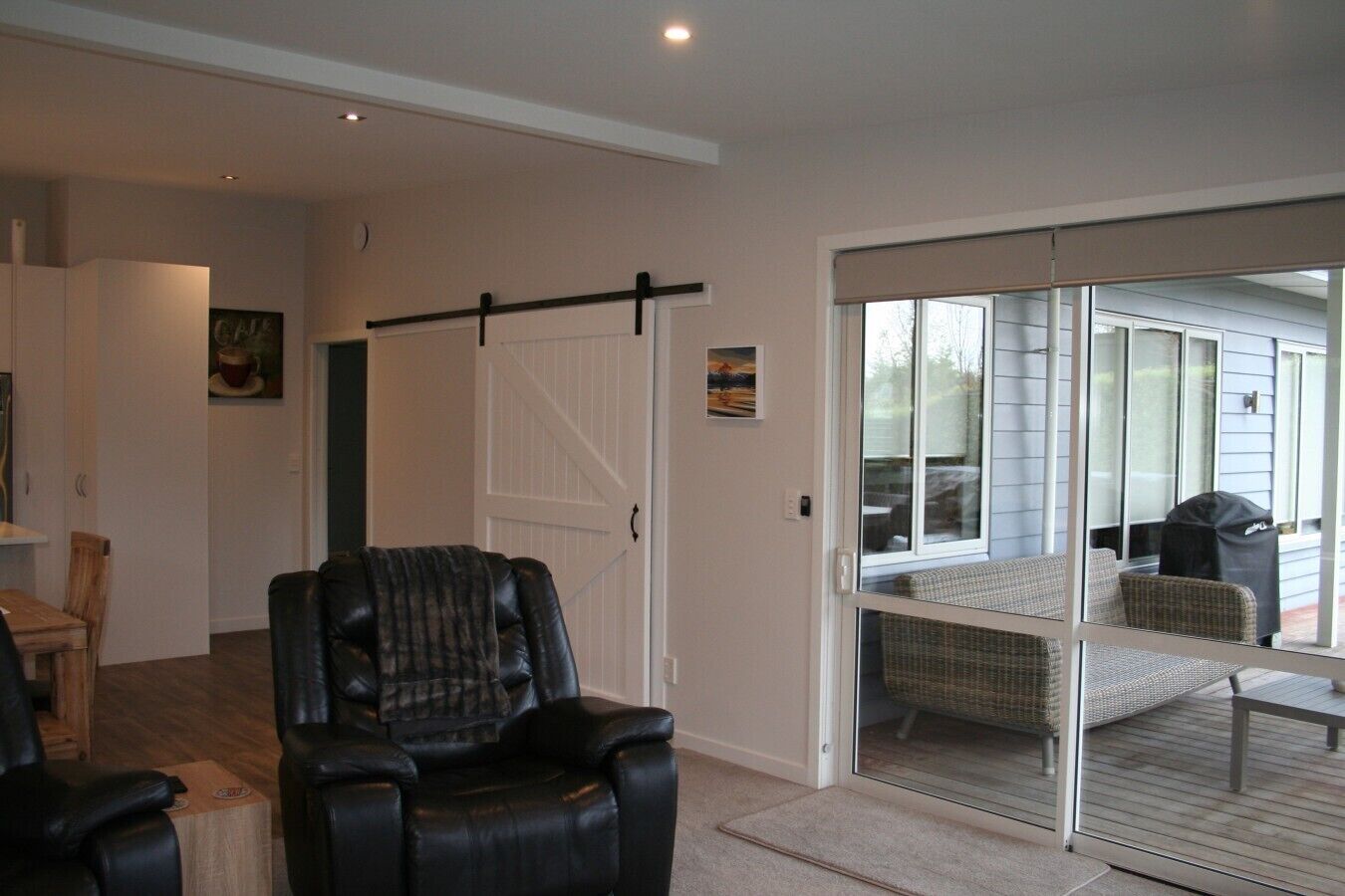 Une pièce dotée d’une porte-fenêtre coulissante donnant sur un patio extérieur, d’un fauteuil en cuir noir et d’une table à manger avec des chaises.