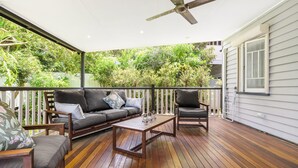 Una terraza techada al aire libre con piso de madera, un ventilador de techo, un sofá, dos sillones y una mesa de centro.