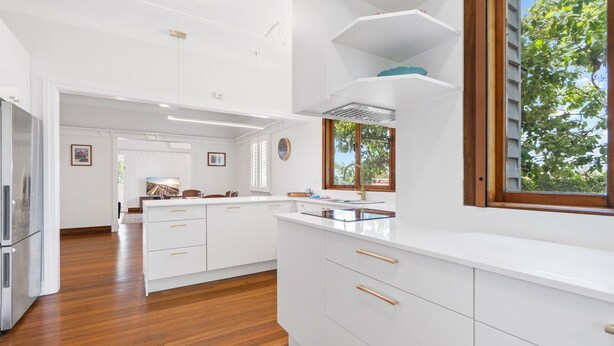 Una cocina moderna con armarios blancos, encimera de madera y ventana con vistas a árboles.