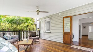 Un espacio exterior techado con una terraza de madera, un sofá, una mesa y un ventilador de techo.