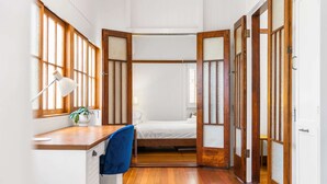 Una habitación con piso de madera, una cama, un escritorio con lámpara y una silla.