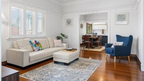 Un salón con un sofá blanco, un sillón azul y un comedor con una mesa y sillas de madera.