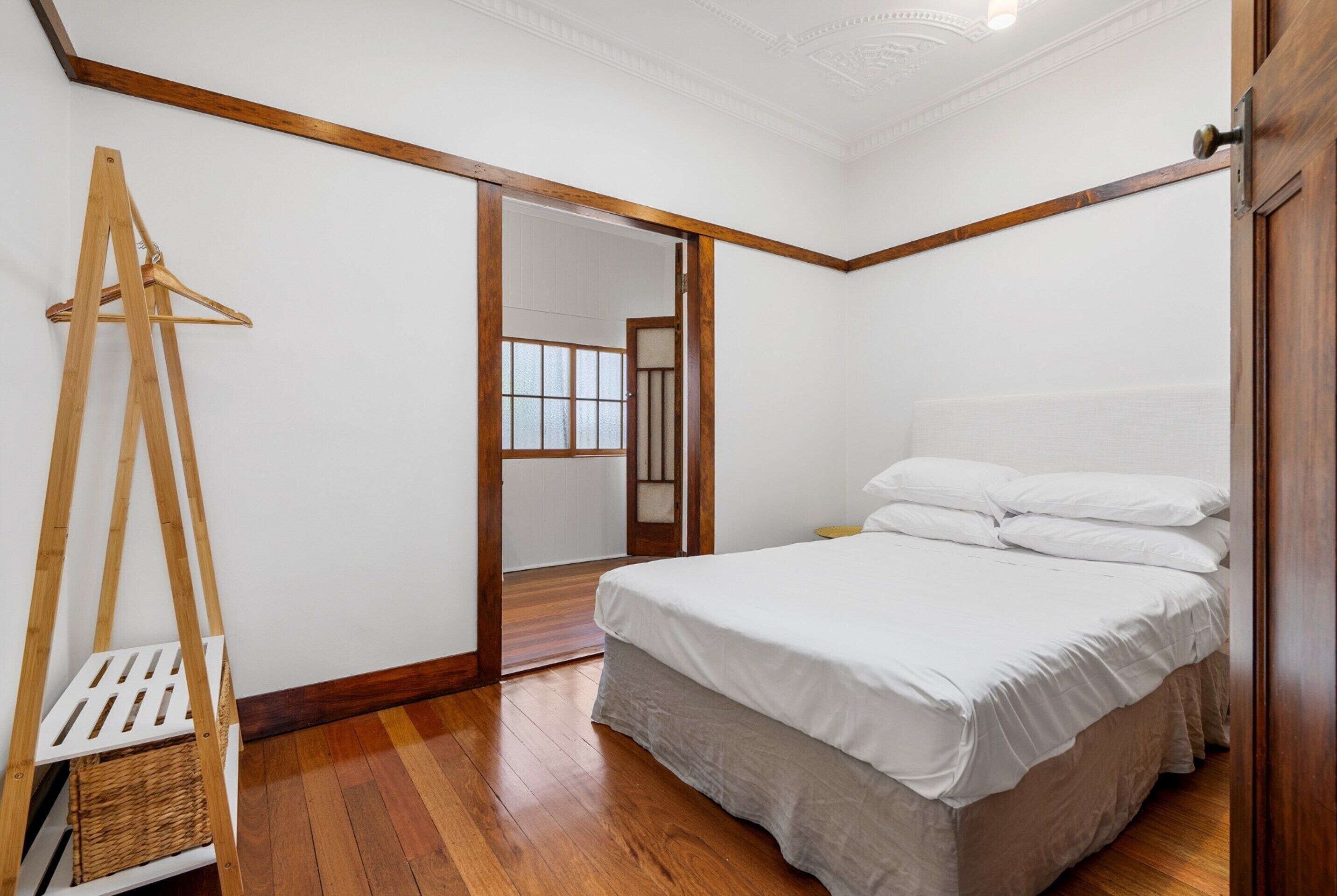 A bedroom with a wooden bed frame, white bedding, a wooden floor, and a wooden wardrobe.