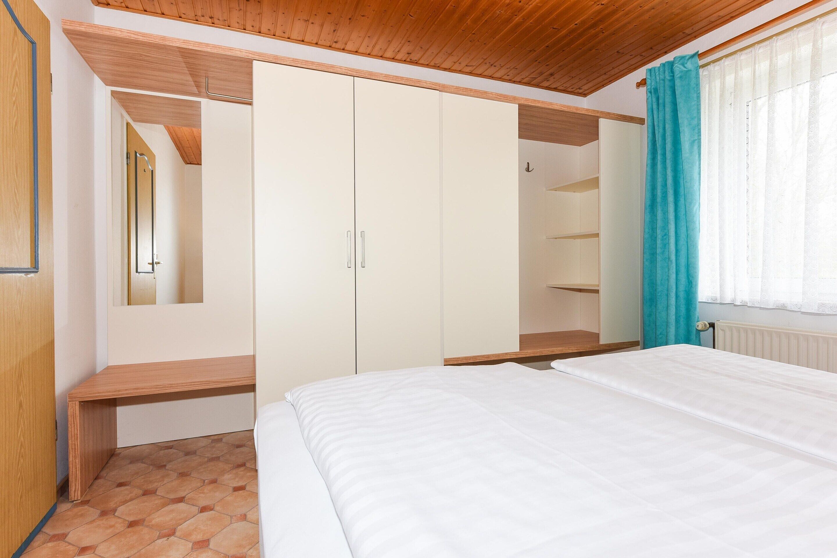 A bedroom with a bed, a wardrobe, a mirror, and a window with curtains.