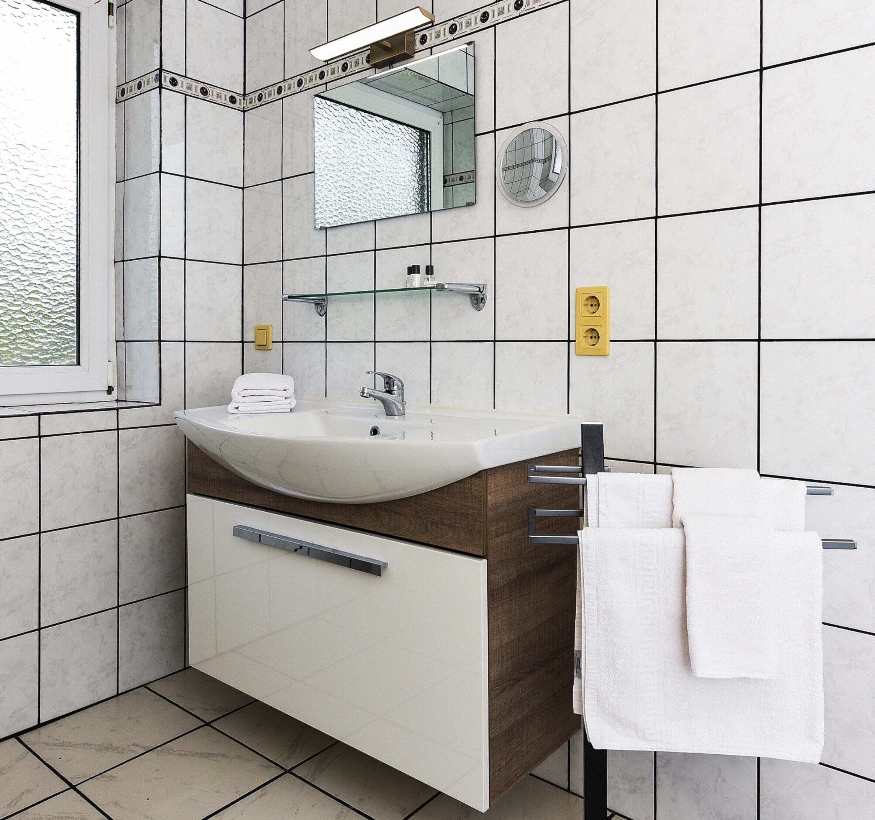 A modern bathroom with a white sink, mirror, and towel rack.