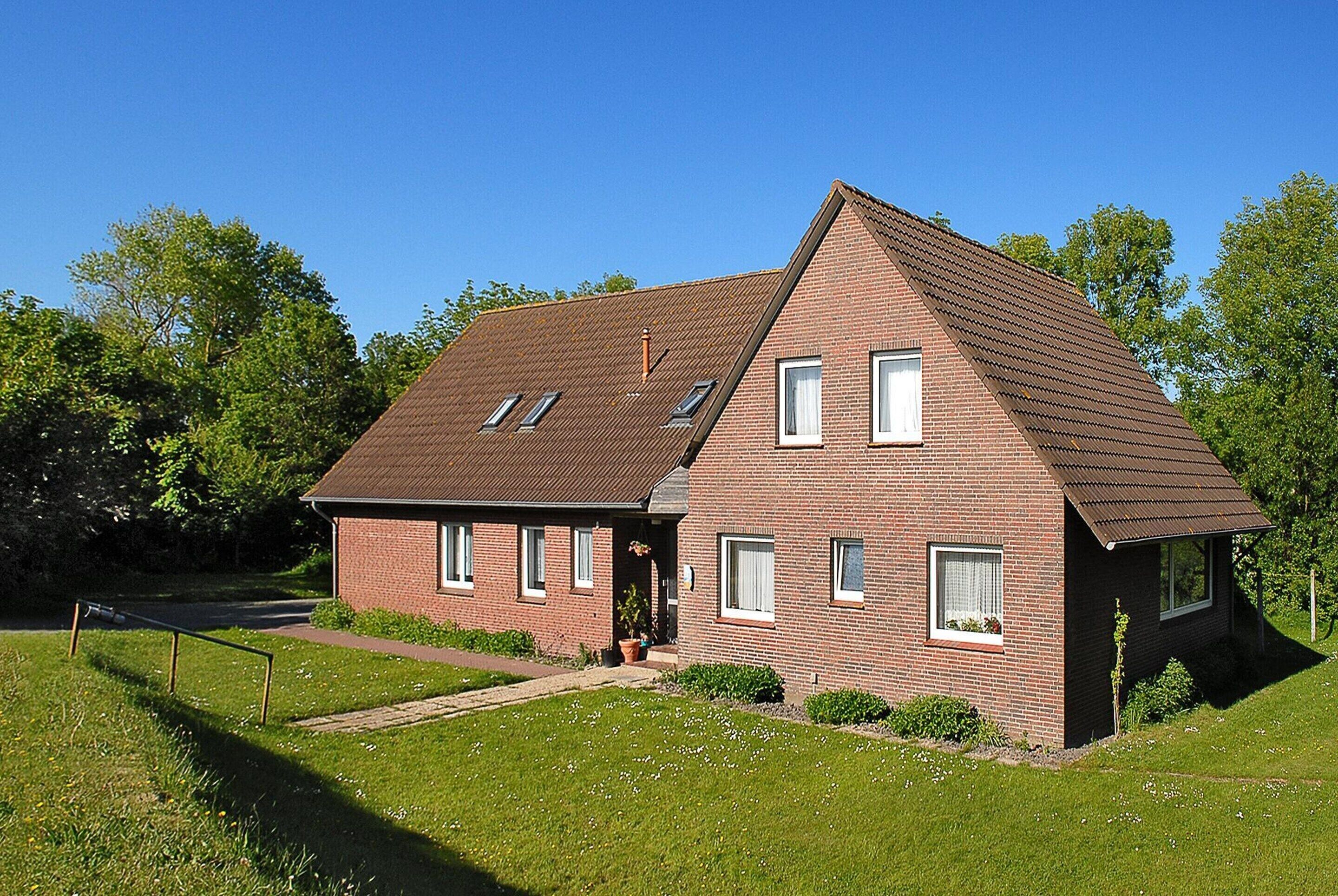 Ein zweistöckiges Backsteinhhaus mit geneigtem Dach, einer Veranda und einem kleinen Garten.