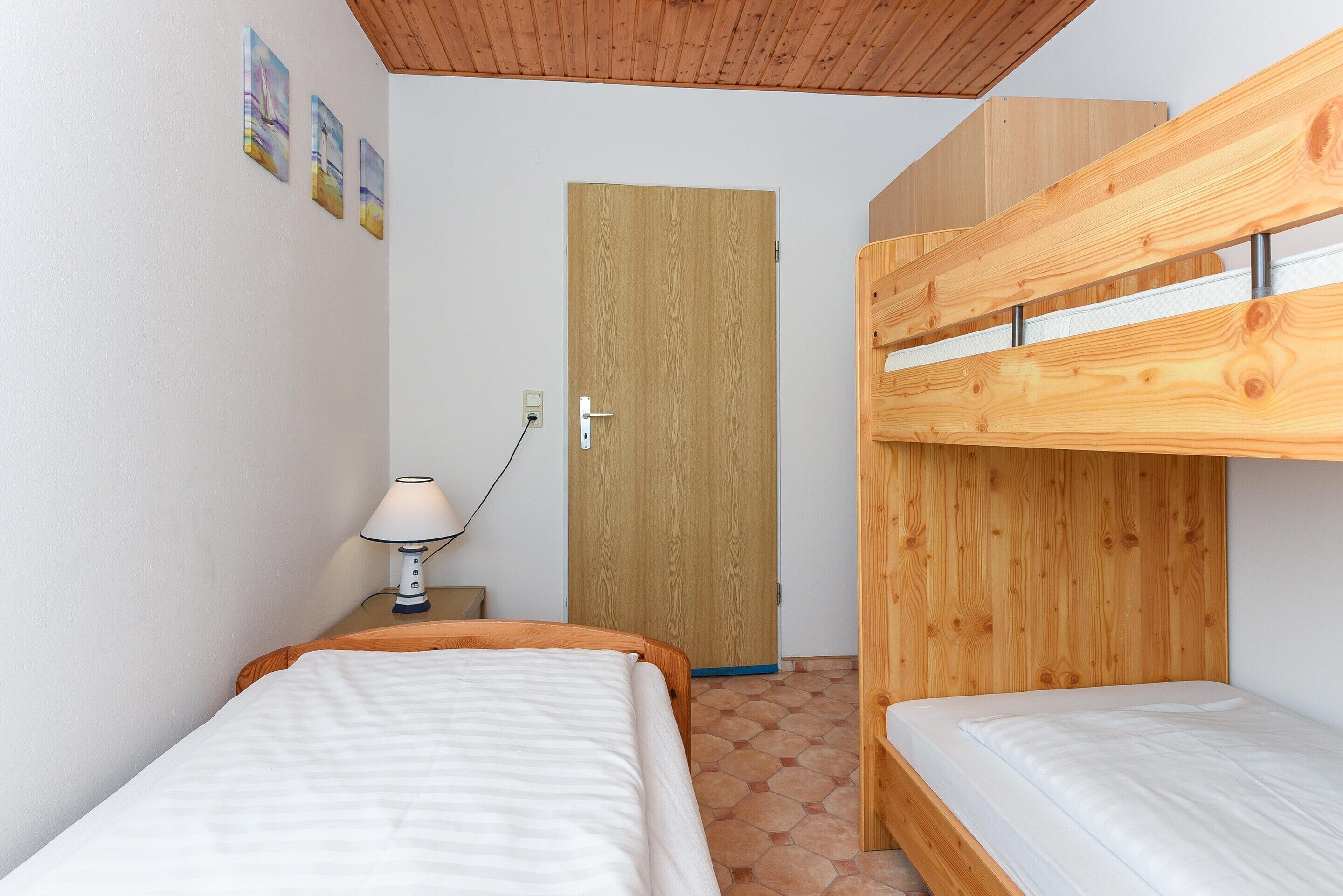 Quarto com uma cama beliche, uma mesinha de cabeceira com abajur e uma porta.