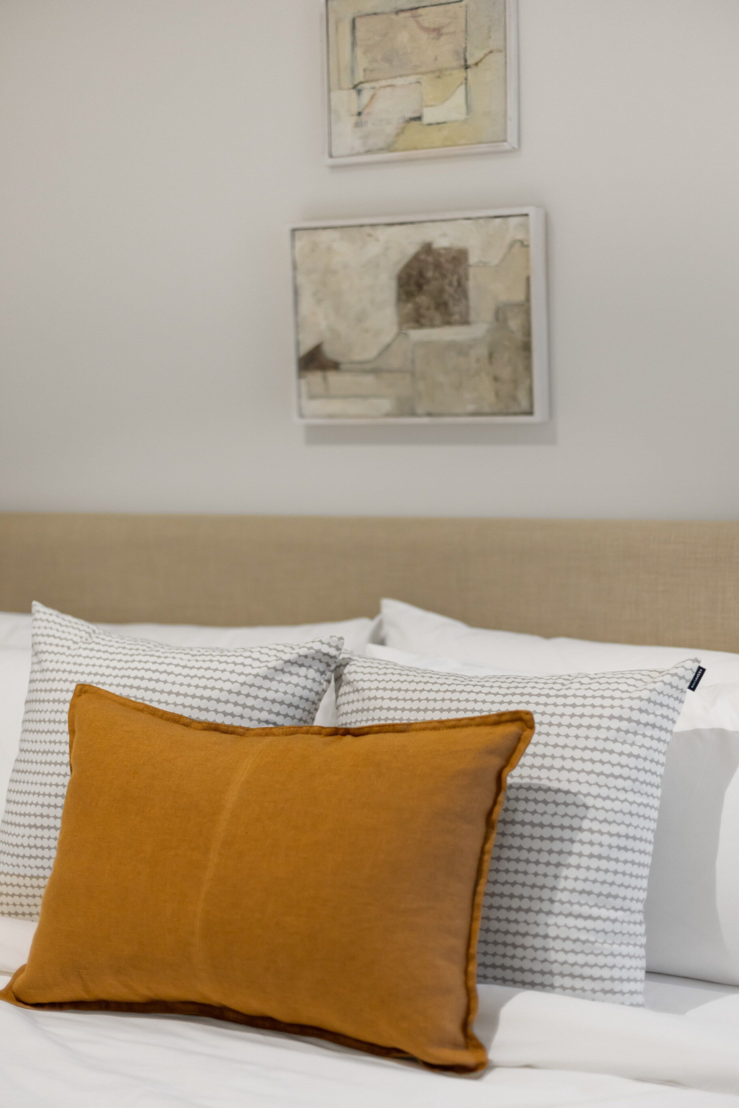 A bed with white bedding and a mustard-colored pillow.