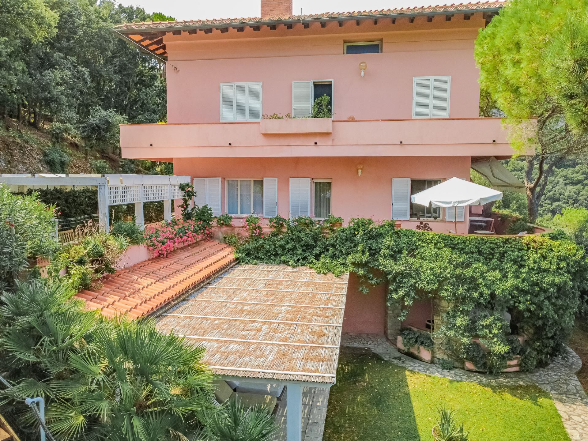 Una casa a due piani con facciata rosa, un portico coperto e un giardino rigoglioso.