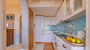 Eine Küche mit weißen Schränken, einer blauen Fliesenrückwand und einer Holzausziehtafel mit Zitronen.