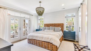 A bedroom with a wicker bed, a nightstand, a dresser, and a chandelier. - Coastal Retreat w/ Private Pool | Golf Cart (Oak Island)