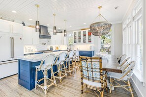 A modern kitchen with white cabinets, a large island, and a dining area with wicker chairs.