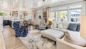 A spacious living room with a large sofa, a coffee table, and a dining area with chairs and a table. - Coastal Retreat w/ Private Pool | Golf Cart (Oak Island)