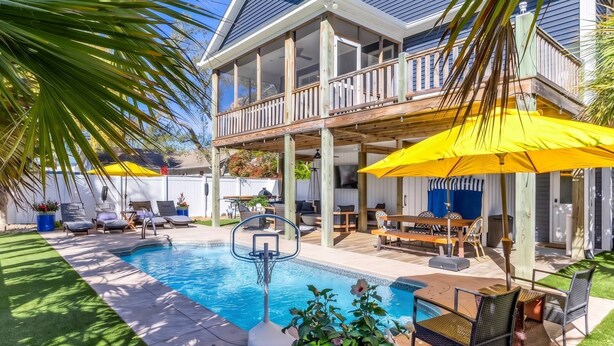 A pool area with a wooden deck, lounge chairs, and umbrellas. - Coastal Retreat w/ Private Pool | Golf Cart (Oak Island)