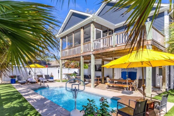 A pool area with a wooden deck, lounge chairs, and umbrellas.