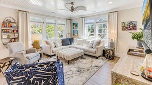 A living room with a sectional sofa, a coffee table, a side table, a bookshelf, and a ceiling fan. - Coastal Retreat w/ Private Pool | Golf Cart (Oak Island)
