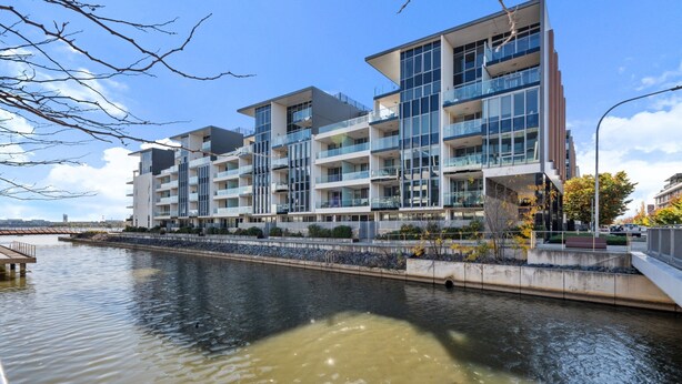 A modern multi-story building with balconies overlooking a body of water. - Spacious Lakefront Apartment With Pool Access (Canberra)