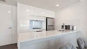A modern kitchen with white cabinetry, a stainless steel refrigerator, a microwave, and a gas stove. - Spacious Lakefront Apartment With Pool Access (Canberra)