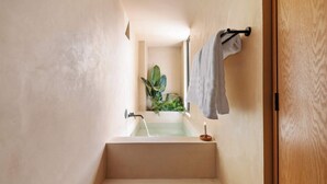 A narrow bathroom with a bathtub, a towel rack, and a plant.