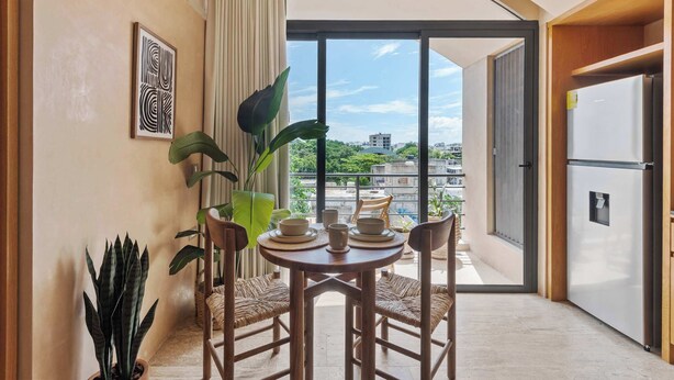 A dining area with a table set for four, a large potted plant, and a view of the city through a glass door.