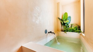 A bathtub with running water, a window with plants, and a plain wall.