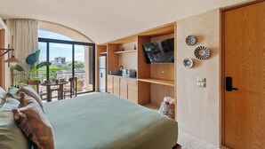 Habitación de hotel con cama, televisión, zona de comedor y vistas a la ciudad.