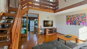 Un'ampia zona giorno con una scala in legno, una televisione e un quadro appeso al muro.