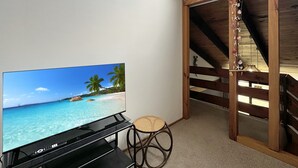 Una stanza con una TV che mostra una spiaggia, una poltrona in vimini e un soffitto in legno.
