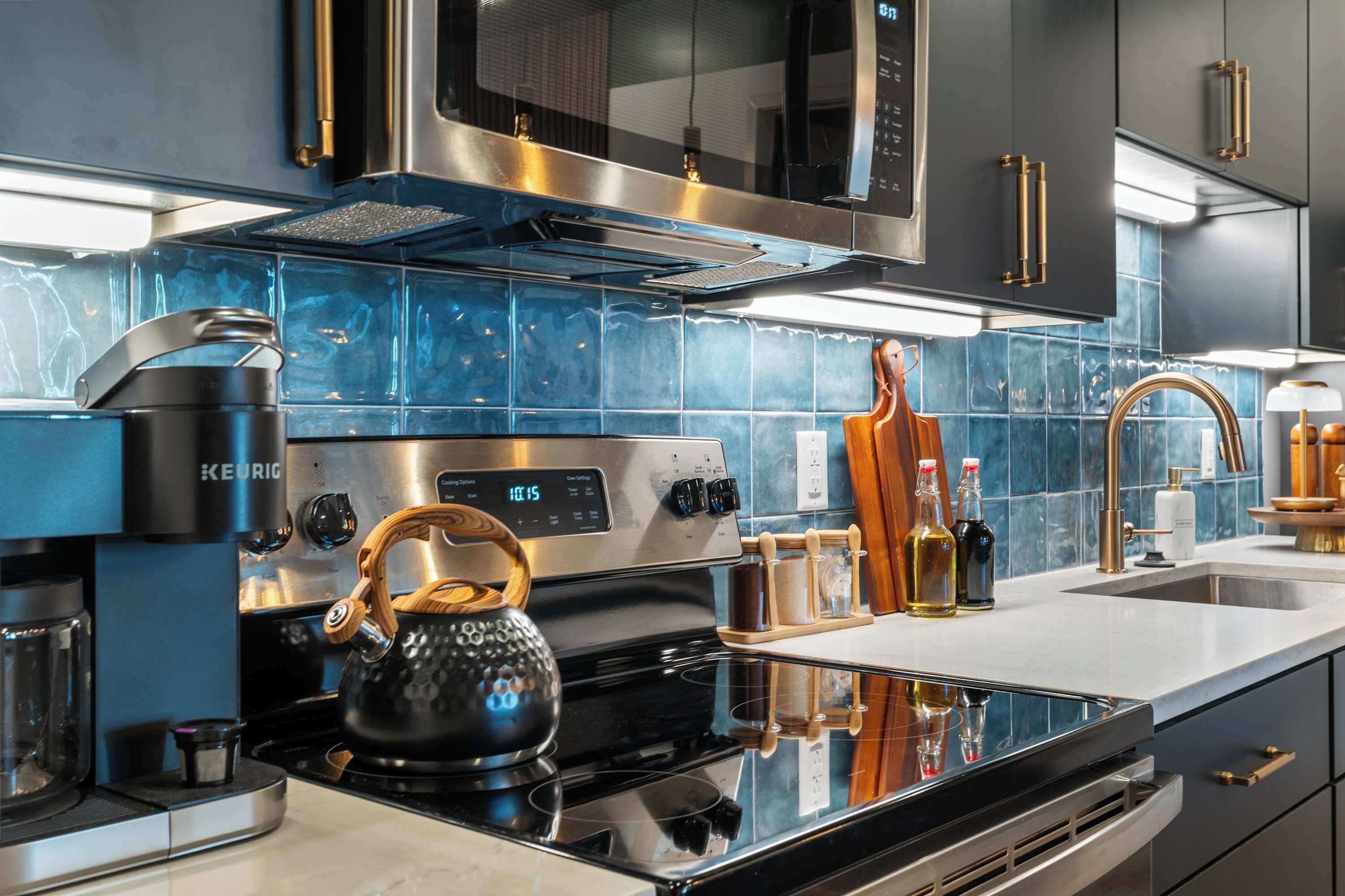 Una cocina moderna con estufa negra, electrodomésticos de acero inoxidable y salpicadero de azulejos azules.