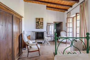 A traditional room with a fireplace, a bed, a chair, and a painting on the wall.