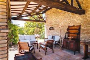 Un patio cubierto con mobiliario de madera, una pared de ladrillo y una lámpara colgante.