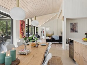 A modern kitchen with a wooden table, white chairs, and a dining area with a view.