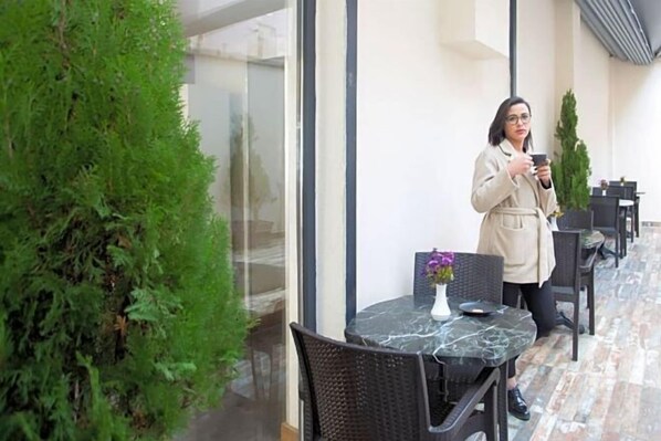 A woman standing by a glass door, holding a cup, in a hallway with a row of tables and chairs. - Sim Hotel Istanbul Old City (Istanbul)