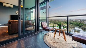 A modern living room with a large glass wall, a leather sofa, a wooden coffee table, and a view of a cityscape.