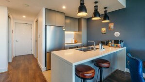 A modern kitchen with a central island, bar stools, pendant lighting, and a refrigerator.