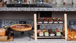 A buffet setup with two coffee dispensers, a pie, assorted desserts, and stacked plates.