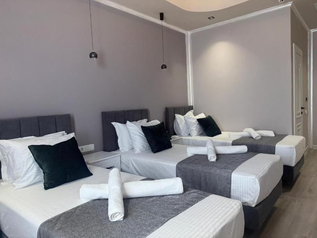 A hotel room with three beds, each with a grey headboard, white bedding, and neatly folded towels.