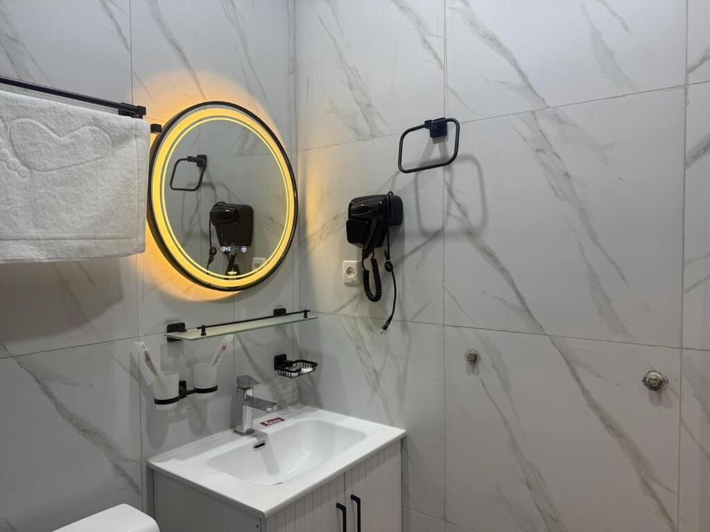 A bathroom with a white sink, a mirror with a circular light, a towel rack, and a handheld showerhead.