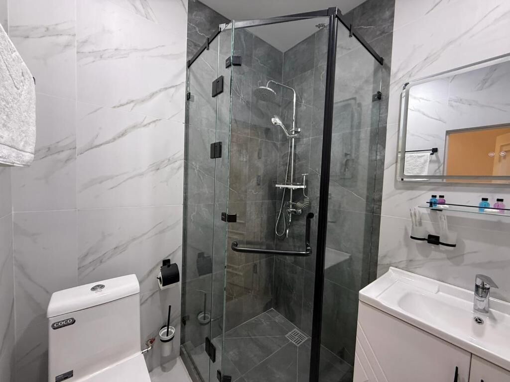 A modern bathroom with a glass-enclosed shower, a white sink, and a marble-tiled wall.