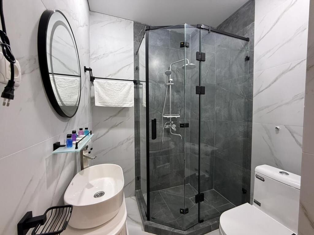 A bathroom with a glass-enclosed shower, a white sink, a toilet, and a mirror.