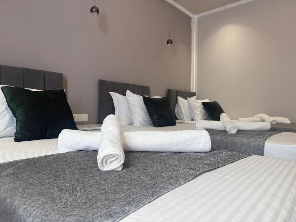 A hotel room with two beds, grey headboards, white and dark grey pillows, and neatly folded white towels.