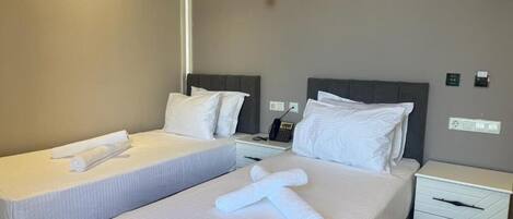 A hotel room with two beds, white linens, bedside tables, and a wall-mounted phone.