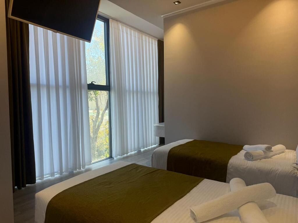 A hotel room with two beds, a TV mounted on the wall, and a window with blinds.