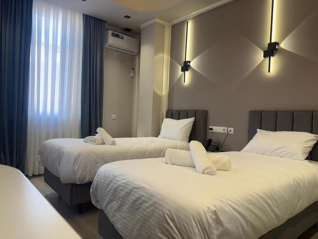 A hotel room with two beds, a wall-mounted air conditioner, and a bedside table with a lamp.